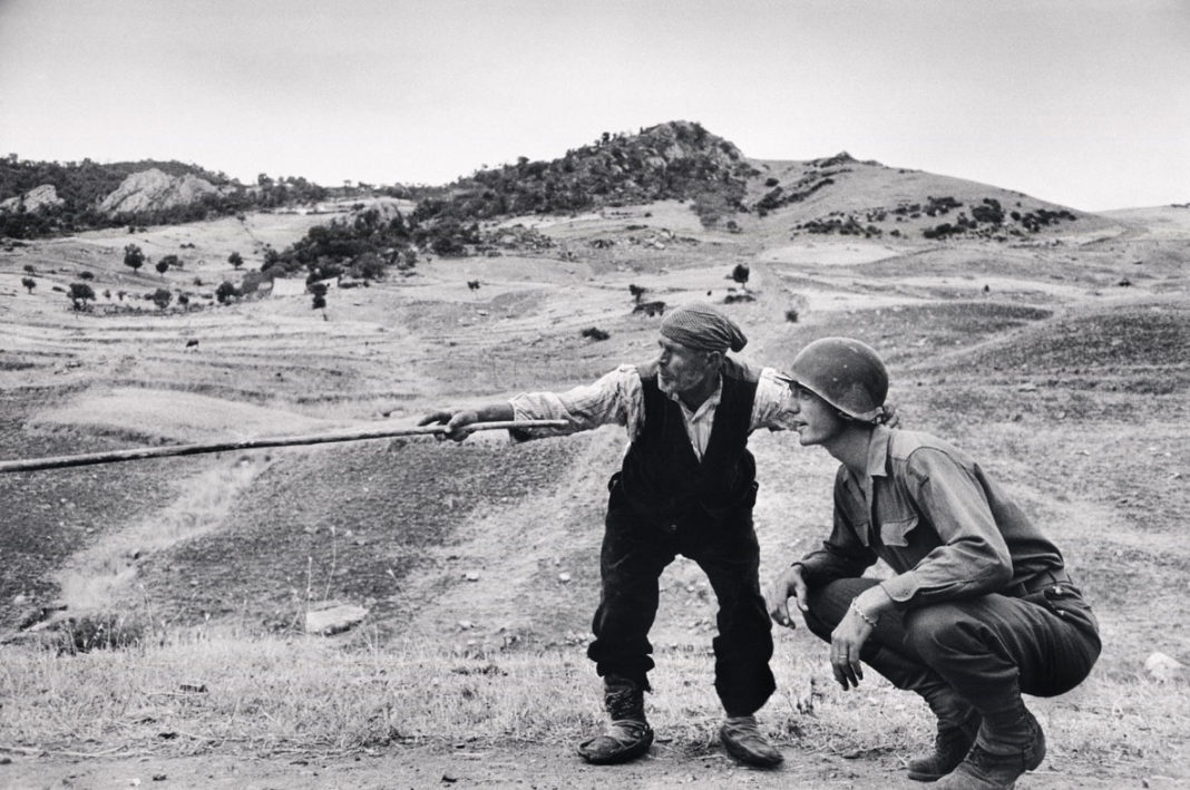 ITALY. Near Troina. August, 1943. Sicilian peasant telling an American officer which way the Germans had gone. ©Robert Capa © International Center of Photography / Magnum Photos